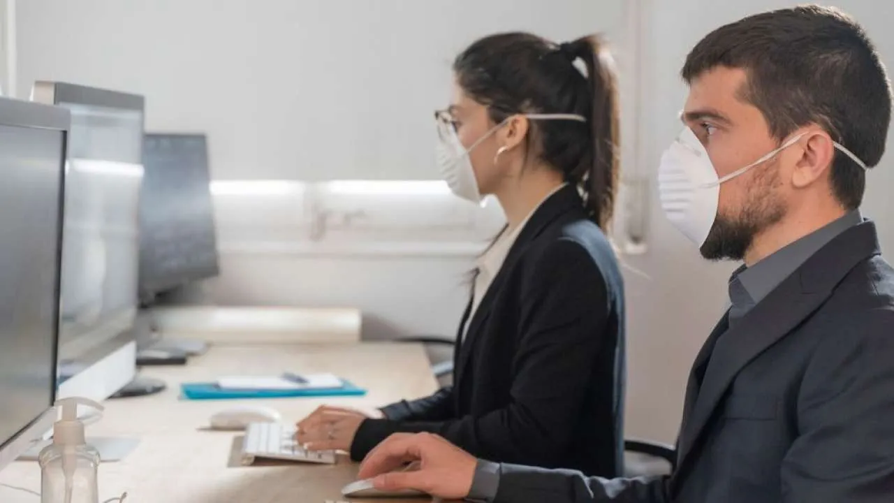 Due impiegati con la mascherina al lavoro davanti a un computer in ufficio