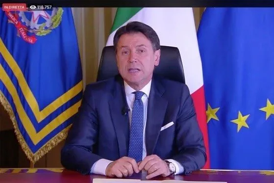Giuseppe Conte durante una diretta istituzionale, seduto fra le bandiere italiana ed europea