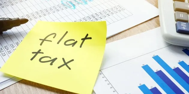 Un foglietto adesivo giallo con la scritta «flat tax» su una scrivania con prospetti e calcolatrice